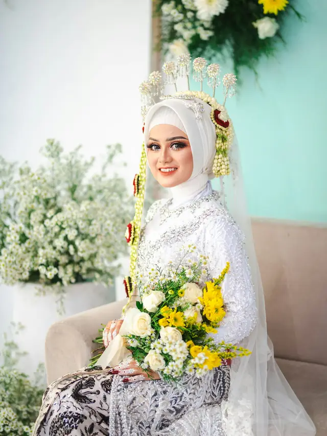 Pengantin berhijab dengan siger, ronce melati, dan buket bunga