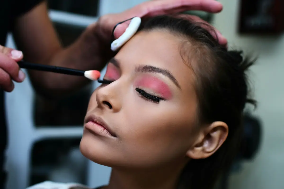 Make-up artist memulas eyeshadow merah muda ke kelopak mata klien