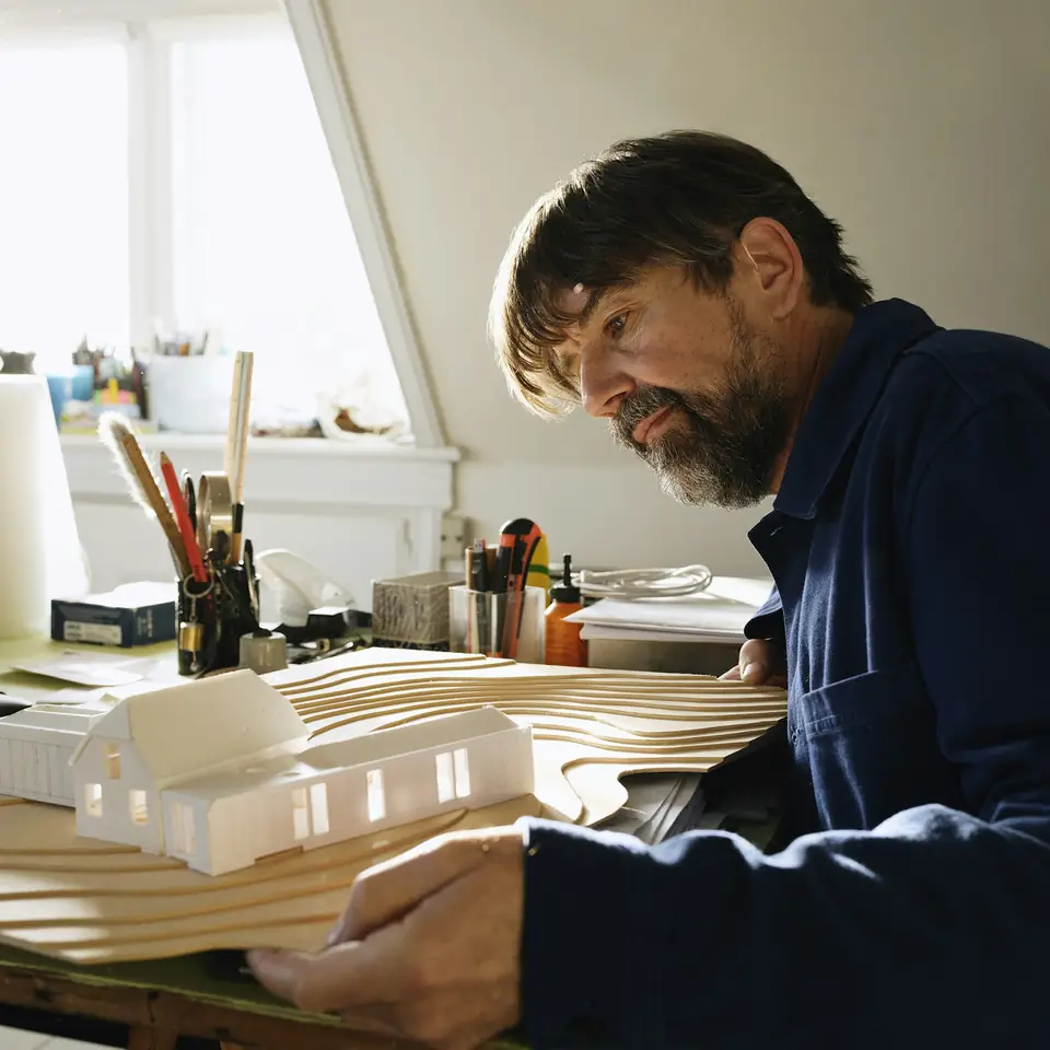 Arsitek mengerjakan maket rumah di mejanya